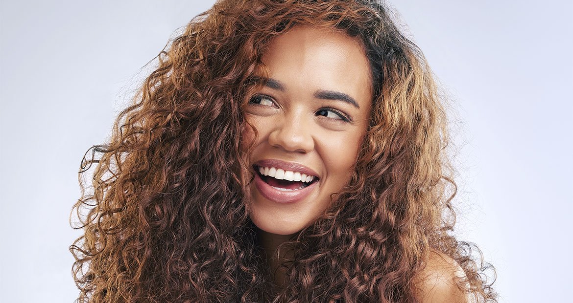 Morena iluminada com cachos longos e volumosos, exibindo um sorriso radiante